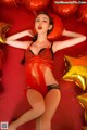 A woman in a red lingerie laying on a red surface surrounded by gold stars.