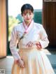 A woman in a white and pink hanbok is posing for a picture.