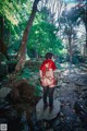 A woman in a red dress is standing on a rock in the woods.