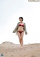 A woman in a red bikini walking on a sandy beach.