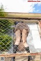 A woman in a skirt and stockings leaning against a fence.