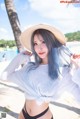 A woman with blue hair wearing a hat on the beach.