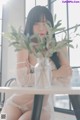 A woman sitting at a table with a plant in a vase.