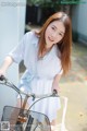 A woman in a white shirt is riding a bike.