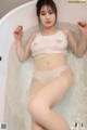 A woman in a white top and panties sitting in a bathtub.