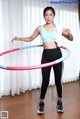 A woman in a blue top and black leggings holding a hula hoop.