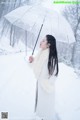 A woman standing in the snow holding an umbrella.