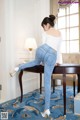 A woman in a white top and blue jeans leaning on a table.