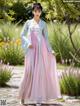 A woman in a pink and blue hanbok standing in a garden.