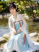 A woman in a blue and white dress sitting by a pond.