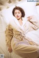 A woman laying on a bed in a beige robe.