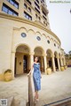 A woman in a blue dress standing in front of a building.